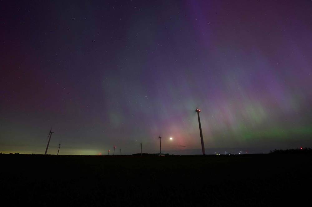 Windmills turn in a field near London, Ontario as the Northern lights or aurora borealis illuminate the night sky during a geomagnetic storm on May 10, 2024. (Photo by Geoff Robins / AFP)