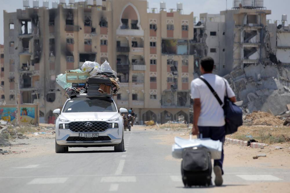 Palestinians who fled Rafah in the southern Gaza Strip carry their belongings from the back of a truck as a man pulls his suitcase upon their arrival to take shelter in Khan Yunis on May 12, 2024. - Photo by AFP
