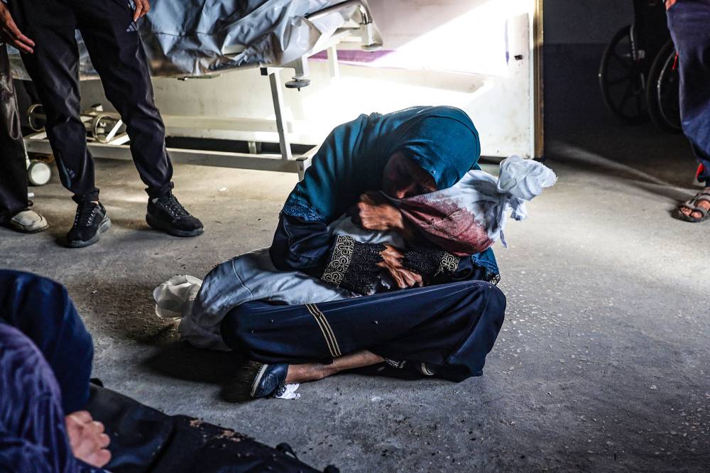 A Palestinian woman holds the shrouded body of child killed in Israeli bombardment, at a health clinic in the area of Tel al-Sultan in Rafah in the southern Gaza Strip on May 26, 2024. - Photo by AFP
