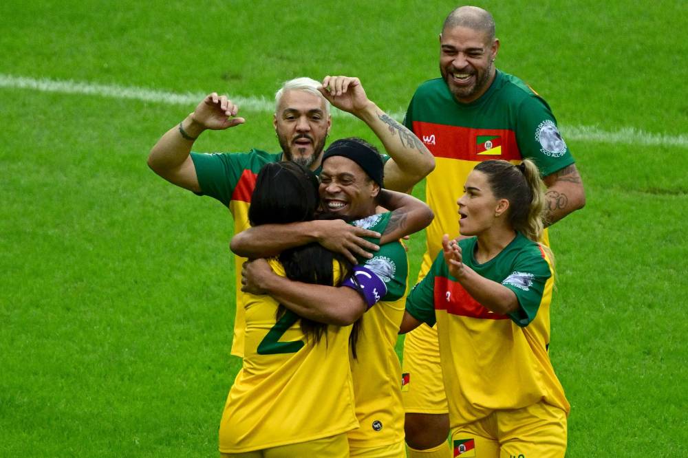 Brazilian singer Ludmilla is embraced by former soccer star Ronaldinho as they celebrate a goal during a charity football match with former football stars and artists at Maracana stadium in Rio de Janeiro on May 26, 2024. - Photo by AFP