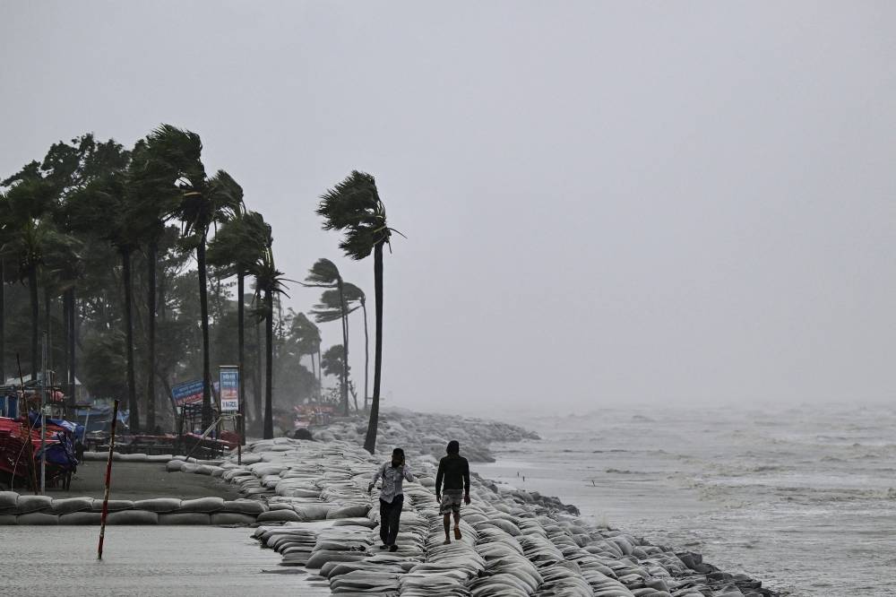 People walk along a beach during rainfall following the landfall of Cyclone Remal in Kuakata on May 27, 2024. Residents of low-lying coastal areas of Bangladesh and India surveyed the damage on May 27 as an intense cyclone weakened into heavy storm, with at least two people dead, roofs ripped off and trees uprooted. - (Photo by MUNIR UZ ZAMAN / AFP)