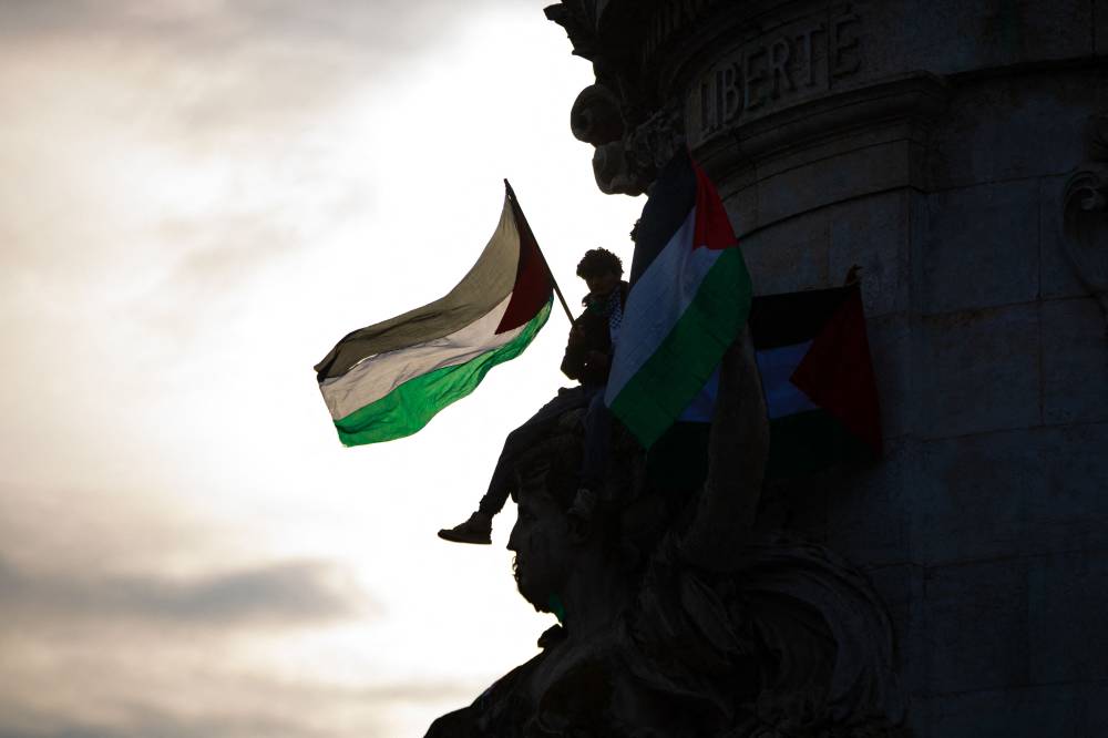 A protester holding palestinian flags sits below the statue "Monument a la Republique" at Place de la Republique, during a demonstration to show support to Palestinians, in Paris on May 28, 2024. - Photo by AFP