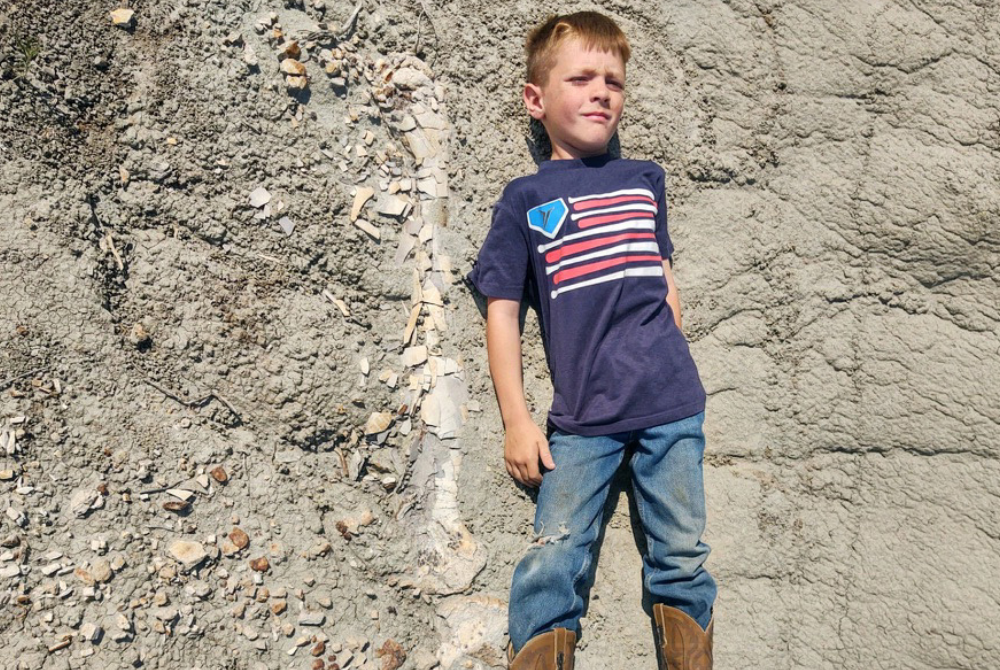 Young Liam Fisher lay down next to the fossilized leg bone of a dinosaur he discovered in the Badlands of North Dakota in 2022, and his family sent the photograph to a paleontologist friend, who confirmed it to be of a juvenile Tyrannosaurus rex. - Photo by AFP