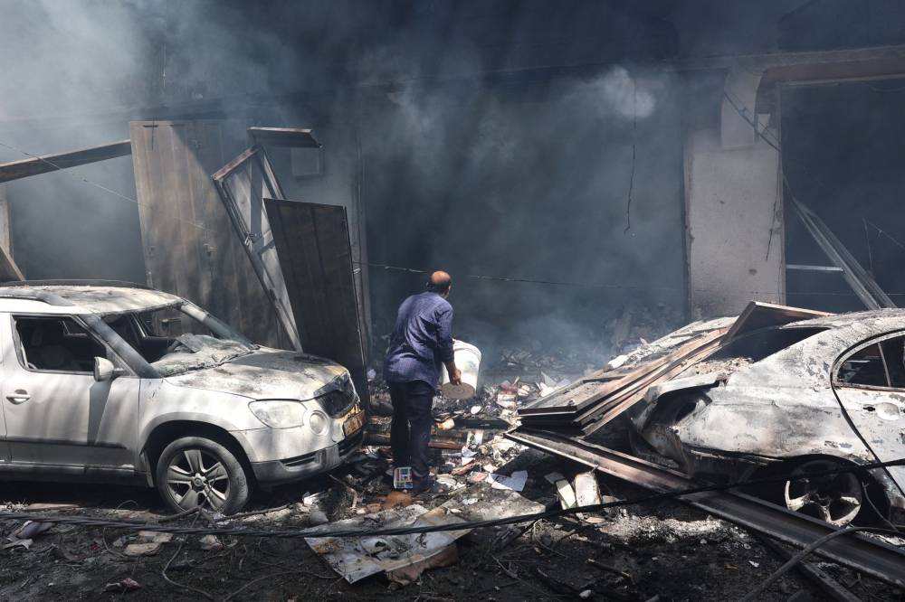 A Palestinian man uses a bucket to douse a smouldering destroyed shop in a building, following an attack by the Israeli Special Forces in the Nuseirat camp, in the central Gaza Strip on June 8, 2024. - Photo by AFP