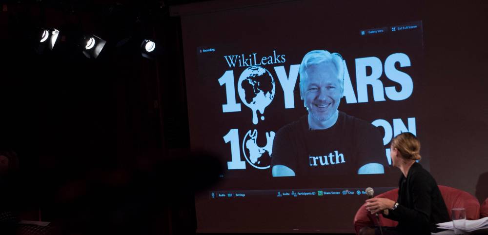 British journalist and WikiLeaks section editor Sarah Harrison (R) looks at a screen displaying Julian Assange, founder of the online leaking platform WikiLeaks, as he addresses journalists via a live video connection during a press conference on the platform's 10th anniversary on October 4, 2016 in Berlin. - File photo by AFP