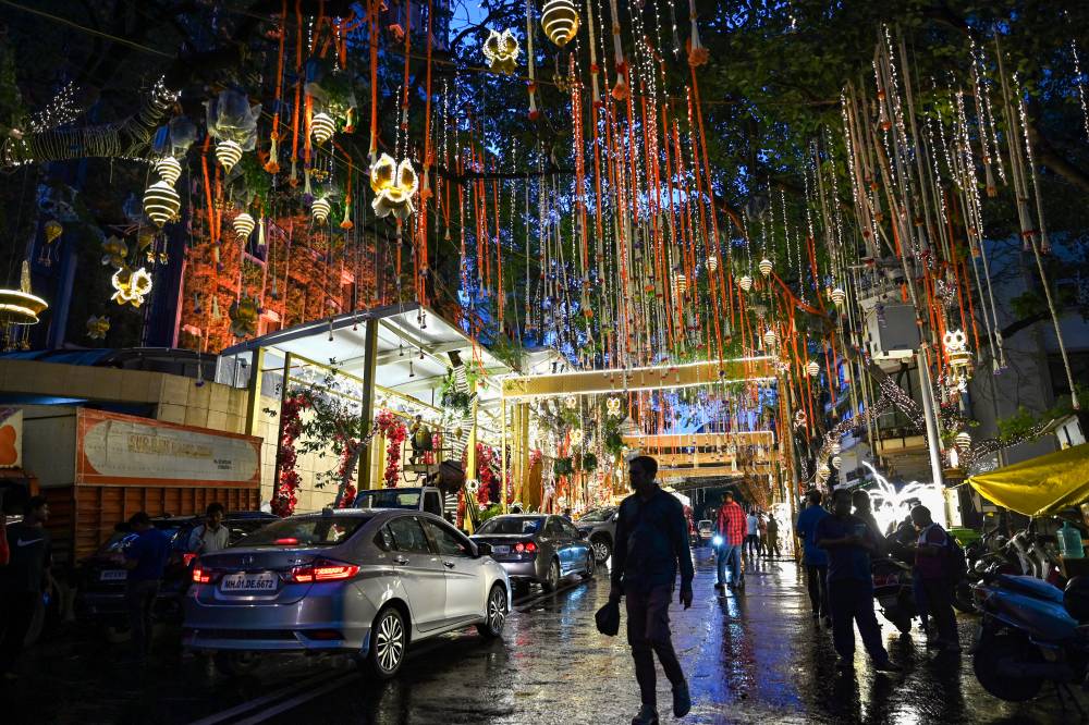 People walk past the Antilia mansion, house of billionaire Mukesh Ambani, while it is lit up ahead of his son Anant Ambani's wedding, in Mumbai on July 9, 2024. (Photo by PUNIT PARANJPE / AFP)