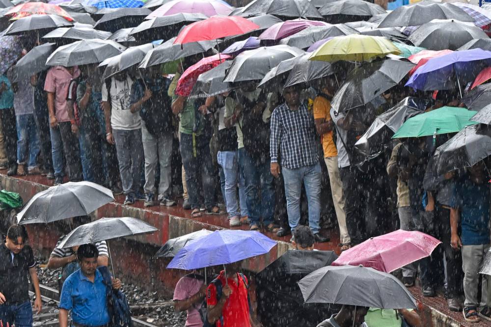 Commuters hold umbrellas as they walk along a railway track amid rainfall in Kolkata on July 12, 2024. (Photo by AFP)