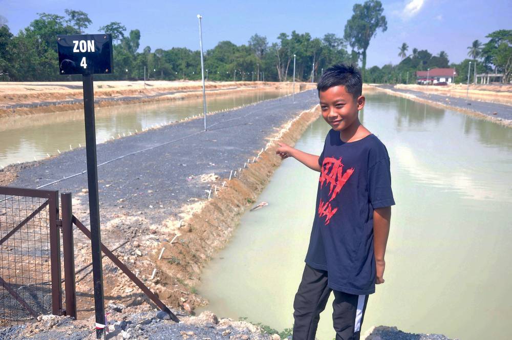 Muhammad Alif Irfan Ahmad Numan points to the location of the fishing competition, where he won the grand prize of RM20,000 in cash recently. The event took place near his home in Kampung Dengir. - Photo by Bernama