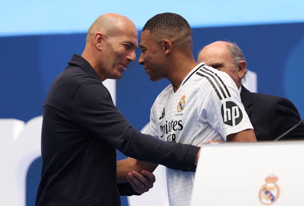 French forward Kylian Mbappe (C) is congratulated by French former football player Zinedine Zidane (L) during a first appearance as a Real Madrid player at the Santiago Bernabeu Stadium in Madrid on July 16, 2024, after signing his new five-season contract. - Photo by AFP