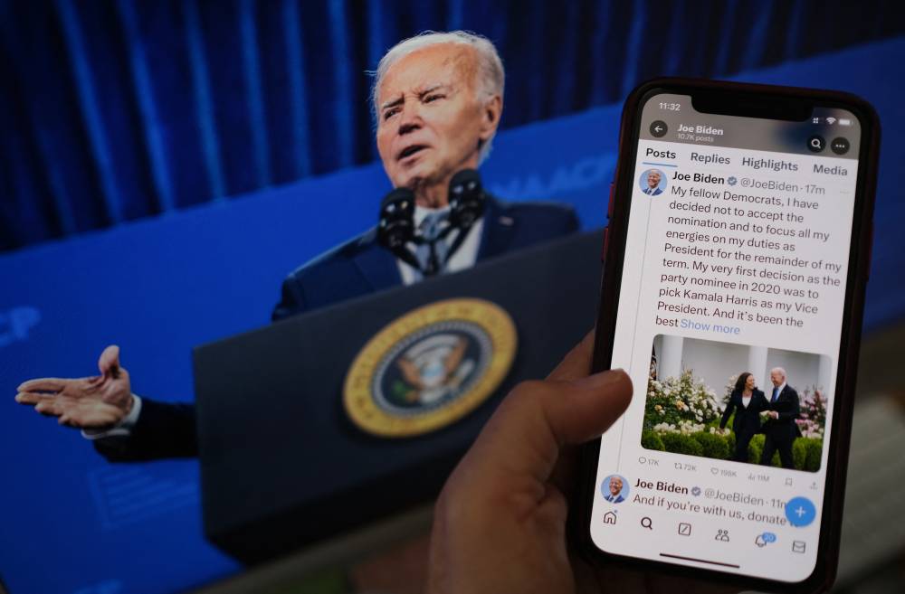 In this illustration photo taken in Los Angeles on July 21, 2024, a person reads the X account of US President Joe Biden announcing he is not accepting the Democratic nomination for the 2024 presidential elections in front of a screen with his photo. (Photo by Chris DELMAS / AFP)