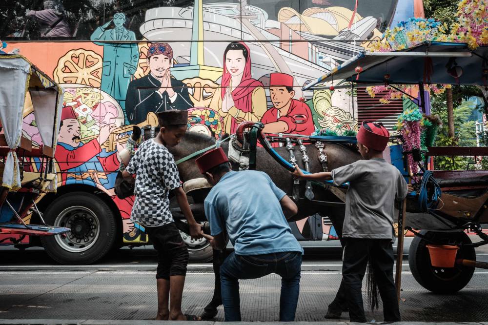 A man repairs the horseshoe of his tourist chariot as a sightseeing bus passes next to the National Monument Park in Jakarta on July 21, 2024. (Photo by AFP)