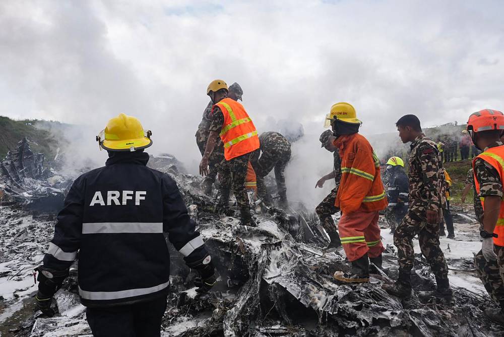 Rescuers and army personnel stand at the site after a Saurya Airlines' plane crashed during takeoff at Tribhuvan International Airport in Kathmandu on July 24, 2024. A passenger plane carrying 19 people crashed during takeoff in Kathmandu on July 24 with the pilot surviving but "many" others aboard dead, police in the Nepali capital told AFP. (Photo by AFP)