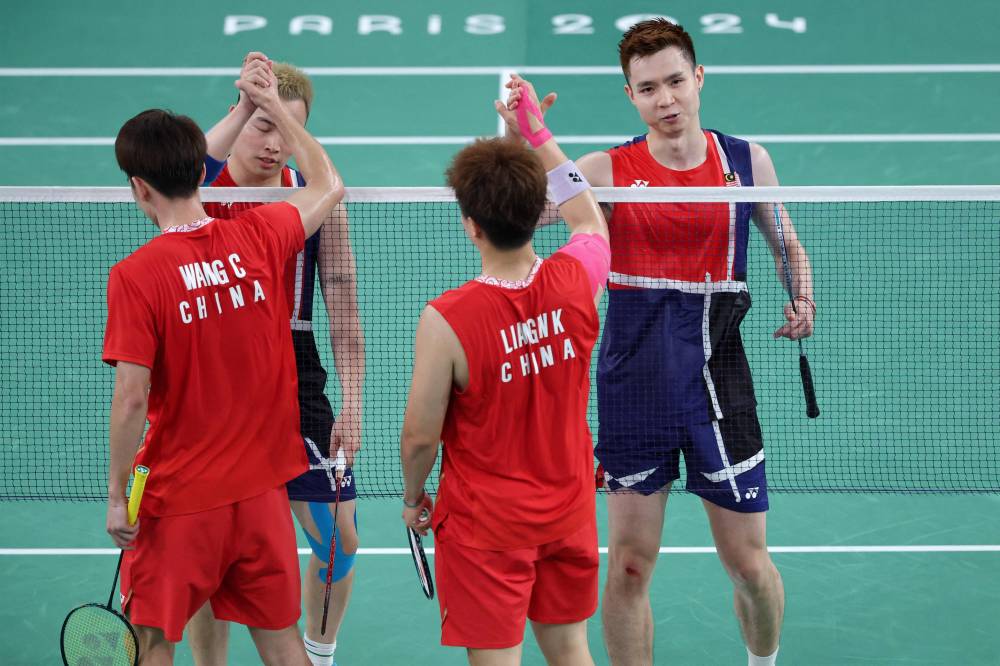 China's Wang Chang and Liang Weikeng shake hands with Malaysia's Aaron Chia and Soh Wooi Yik after their mixed doubles badminton group stage match during the Paris 2024 Olympic Games at Porte de la Chapelle Arena in Paris on July 29, 2024. (Photo by AFP)