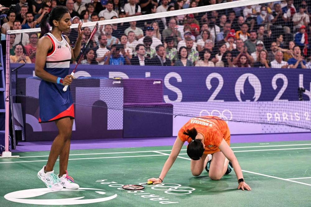Japan's Wakana Nagahara reacts on the ground behind the net next to Malaysia's Muralitharan Thinaah in the women's doubles badminton group stage match during the Paris 2024 Olympic Games at Porte de la Chapelle Arena in Paris on July 28, 2024. (Photo by AFP)