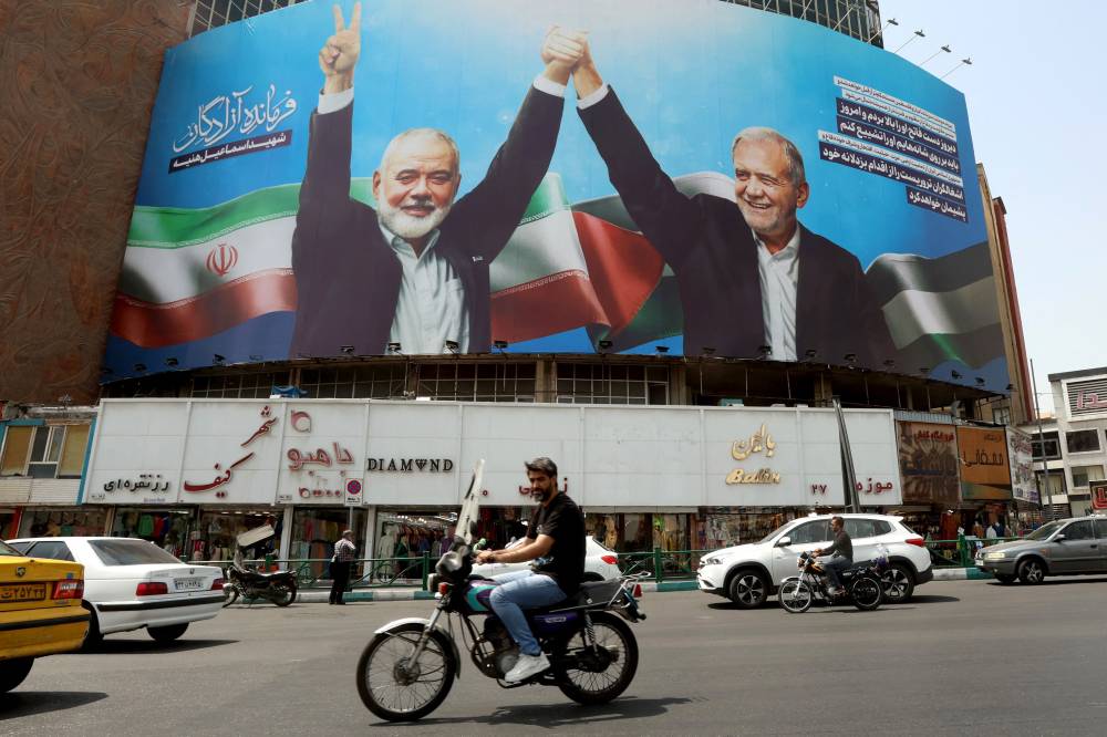 Iranians drive next to a billboard of Iranian president Masoud Pezeshkian (right) and late Hamas leader Ismail Haniyeh at the Valise square in Tehran. Photo by AFP