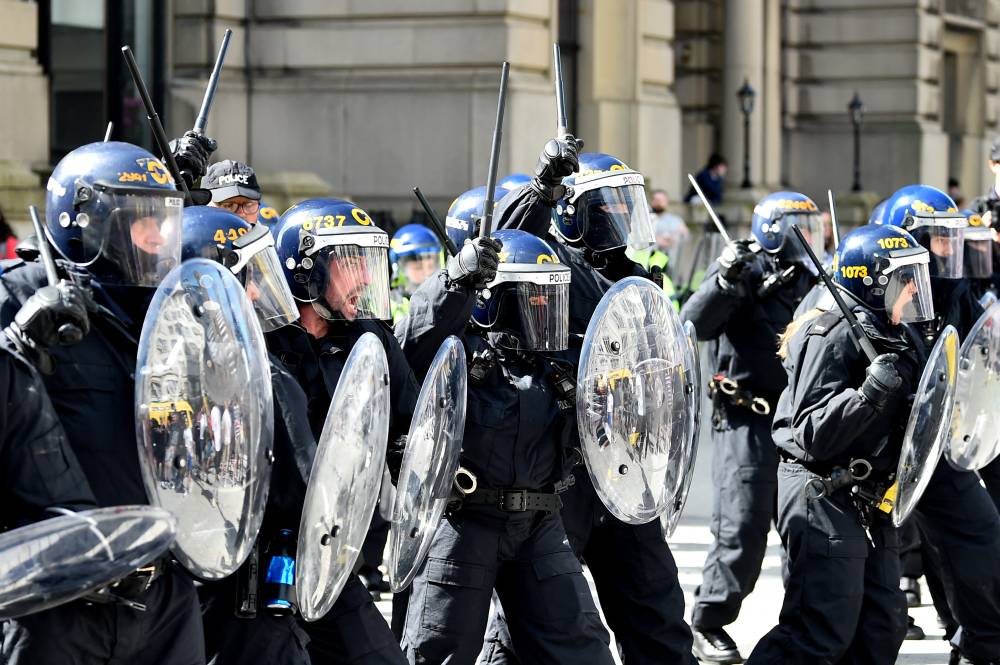 Police officers in riot gear gesture with batons during the 'Enough is Enough' demonstration held in reaction to the fatal stabbings in Southport on July 29, outside the Liver Building in Liverpool on Aug 3, 2024. - (Photo by PETER POWELL / AFP)