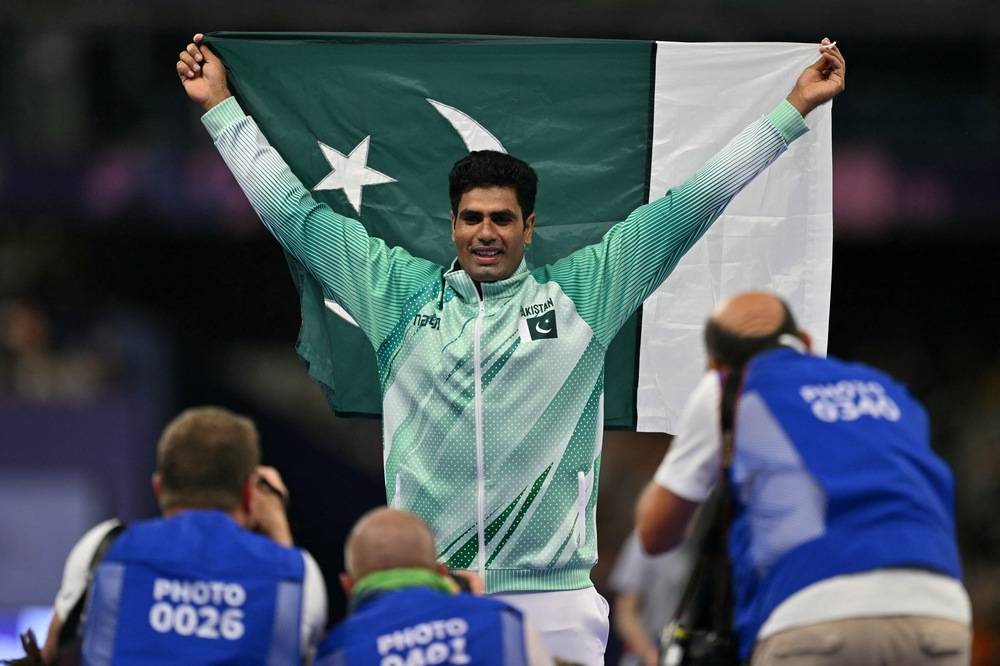 Gold medallist Pakistan's Arshad Nadeem poses with his national flag in front of photographers as he celebrates winning the men's javelin throw final of the athletics event at the Paris 2024 Olympic Games at Stade de France in Saint-Denis, north of Paris, on Aug 8, 2024. (Photo by AFP)