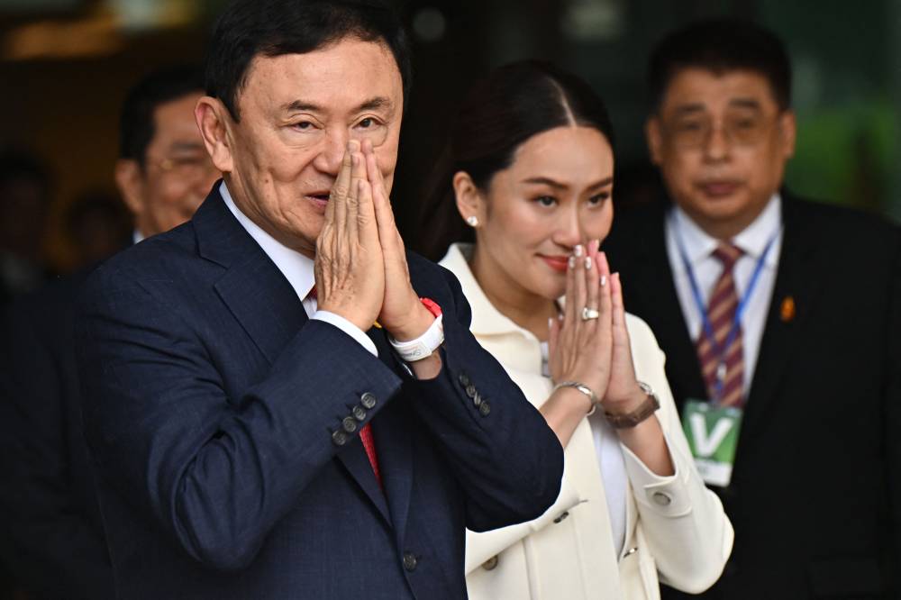 Former Thai Prime Minister Thaksin Shinawatra greets his supporters with his youngest daughter Paetongtarn Shinawatra (R) after landing at Bangkok's Don Mueang airport on August 22, 2023. - File photo by AFP