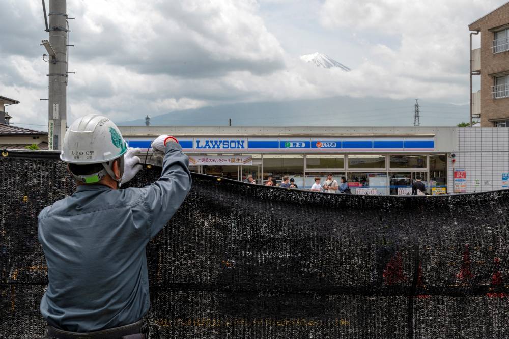 This photo taken on May 21, 2024 shows a worker installing a barrier to block the sight of Japan's Mount Fuji emerging from behind a convenience store to deter badly behaved tourists, in the town of Fujikawaguchiko, Yamanashi prefecture. - (Photo by KAZUHIRO NOGI / AFP)