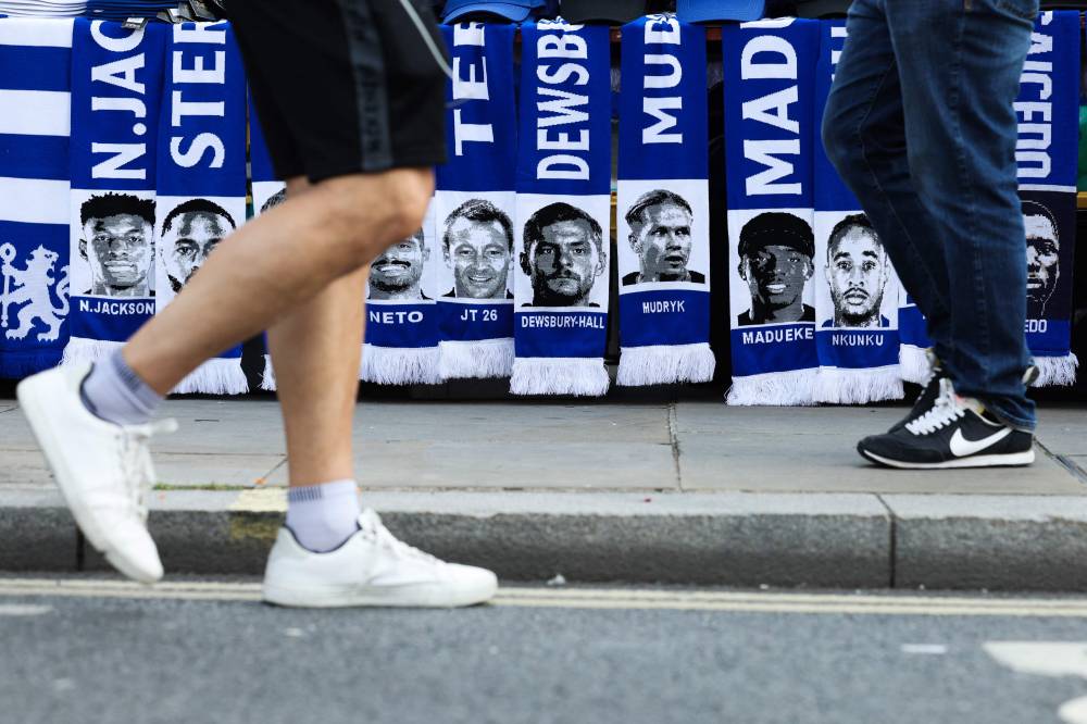 People walk past Chelsea scarves upon their arrival to attend the English Premier League football match between Chelsea and Manchester City at Stamford Bridge in London on August 18, 2024. (Photo by AFP) - Photo by AFP