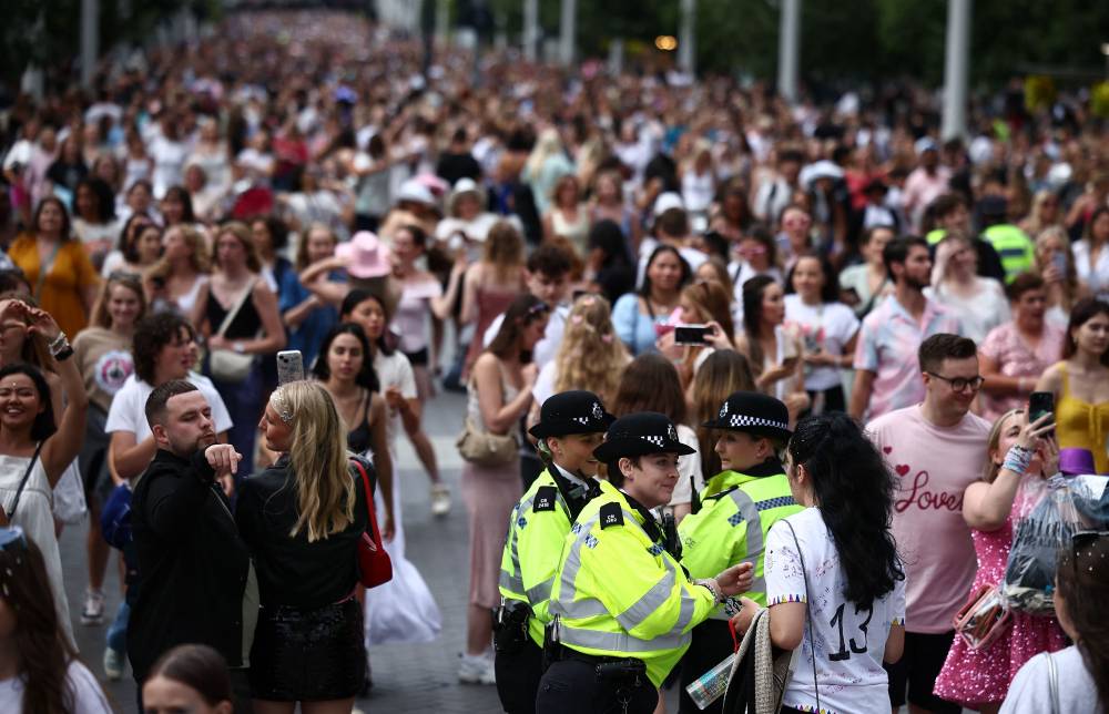 Police officers talk with fans of US mega-star Taylor Swift, so-called "Swifties", as they walk along Olympic Way outside Wembley Stadium in London on August 15, 2024. - Photo by AFP