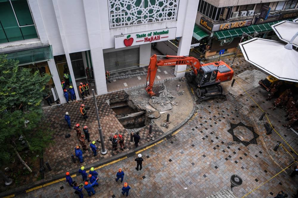 Fire and Rescue Department personnel actively working to rescue a tourist who fell into a sinkhole that opened up at her feet in Jalan Masjid India, today. - Photo by Bernama