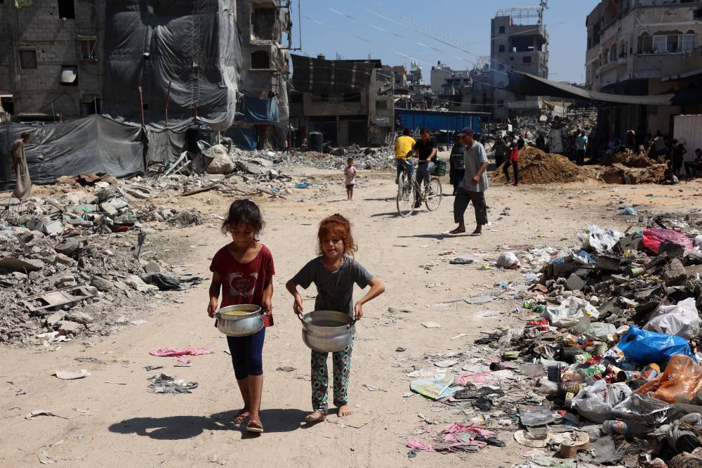 Palestinian children carry pots of soup near a food distribution point in the Jabalia refugee camp in northern Gaza Strip on Aug 21, 2024. - (Photo by OMAR AL-QATTAA / AFP)