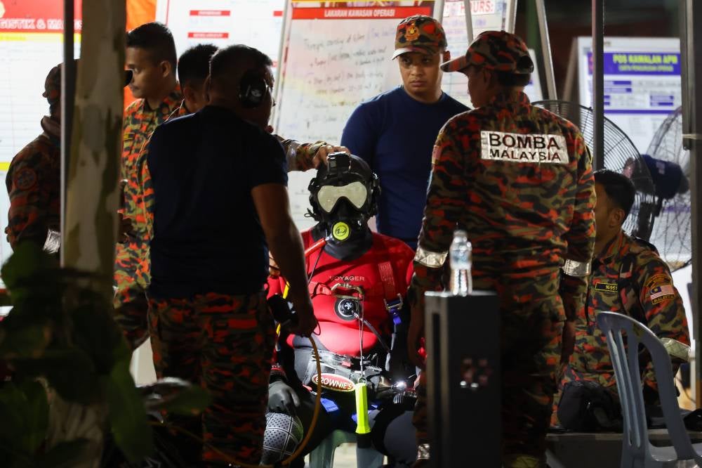 Two firemen from the Malaysian Fire and Rescue Department Diving Team who were fully equipped with scuba gear were seen descending into the hole at 3.06am. Photo by Bernama