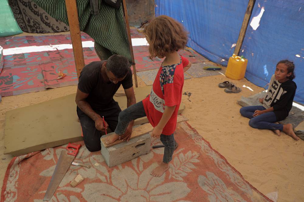 Saber Dawas makes wooden slippers for a displaced child in the al-Mawasi area of the southern Gaza. Photo by Rizek Abdeljawad/Xinhua