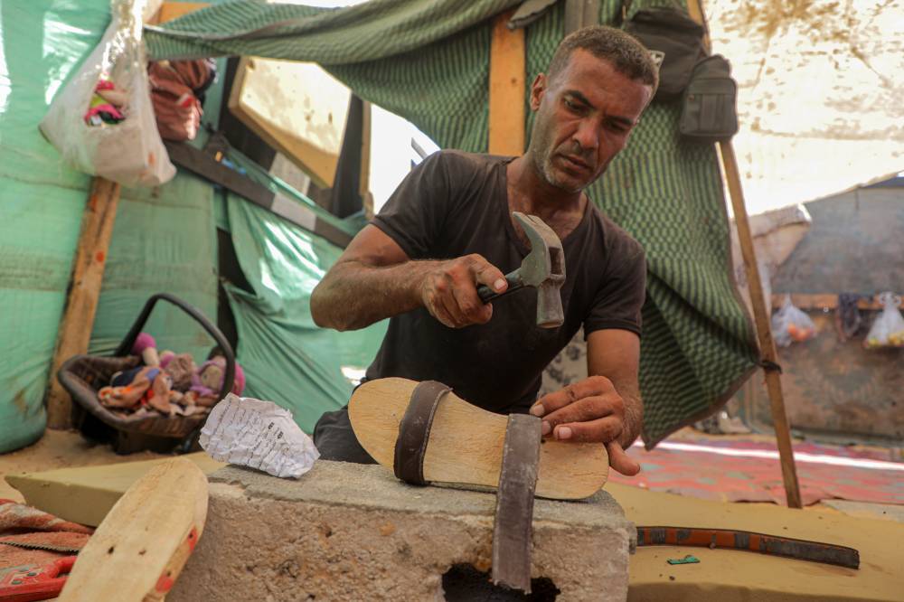 Saber Dawas makes wooden slippers for a displaced child in the al-Mawasi area of the southern Gaza Strip city of Khan Younis. Photo by Rizek Abdeljawad/Xinhua