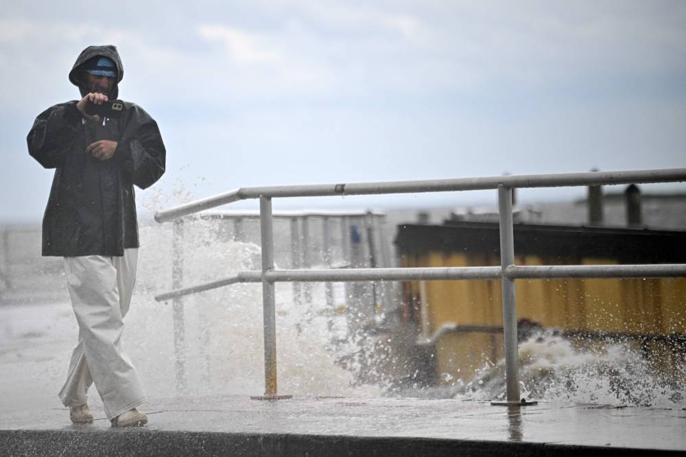 A man uses his phone as waves crash againstthe shoreline ahead of the arrival of Hurricane Helene in Cedar Key, Florida, on September 26, 2024. - Photo by AFP