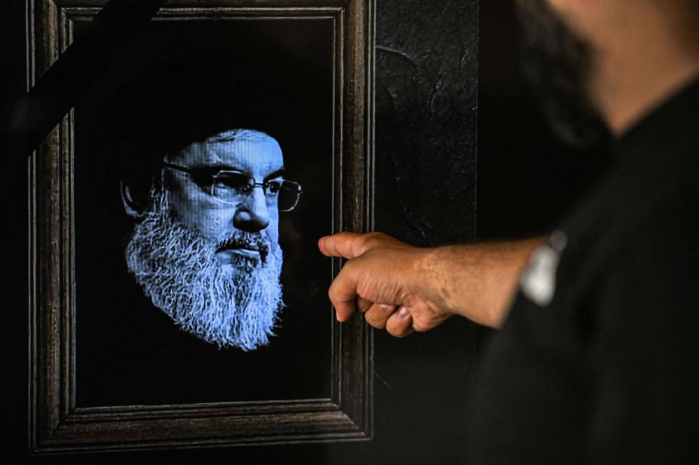 A man points to a television set displaying an image of the late leader of Hezbollah Hassan Nasrallah with a black stripe for mourning during a broadcast from the private Lebanese station NBN in Beirut on September 28, 2024. - Photo by AFP