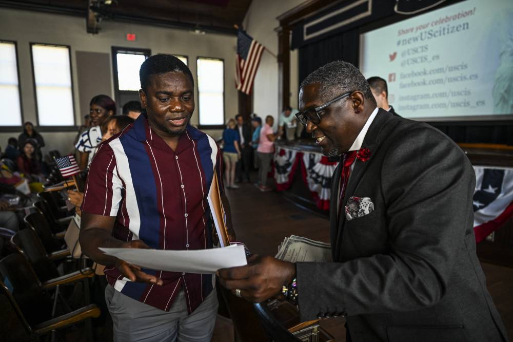 Rhomello Saddiq (R), Supervisory Immigration Services Officer, USCIS Atlanta, presents citizenship certifications to new citizens during a naturalization ceremony for 100 new citizens in celebration of former US President Jimmy Carter's 100th birthday, at Plains High School in Plains, Georgia, on October 1, 2024. (Photo by CHANDAN KHANNA / AFP)