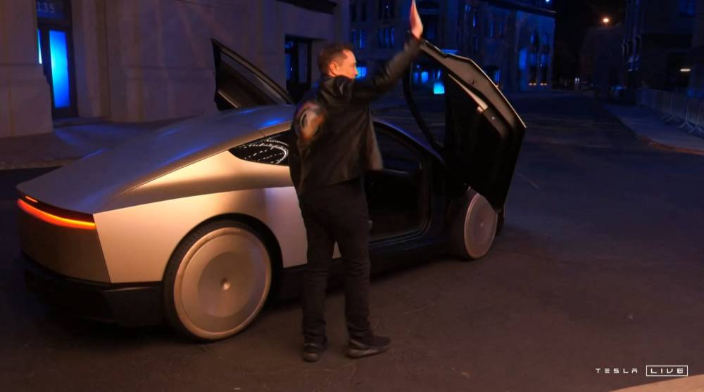 Video grab obtained 10 October, 2024 shows Tesla CEO Elon Musk waving next to his long-promised robotaxi during a launch event at the Warner Brothers studio lot near Los Angeles. (Photo by Tesla/AFP)