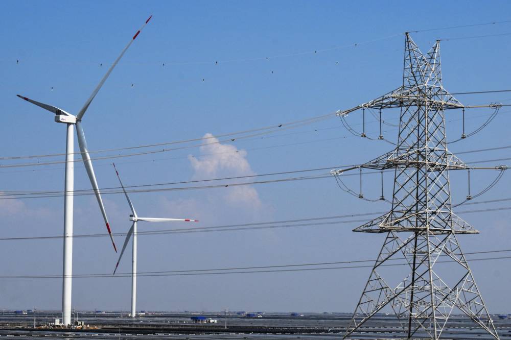 An electricity transmission tower and wind turbines are pictured at the Adani Green Renewable Energy Plant in Khavda, in India's Gujarat state on October 15, 2024. (Photo by Punit PARANJPE / AFP)