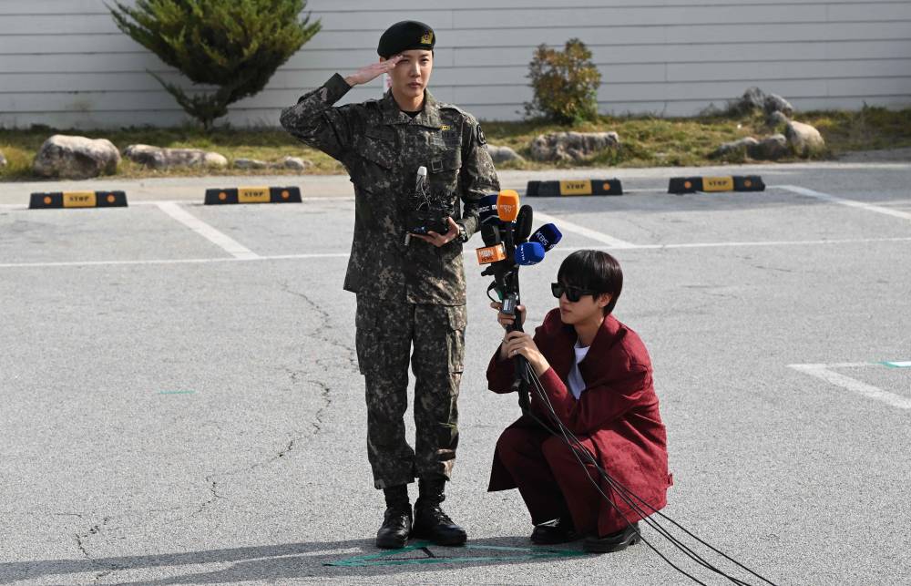 BTS member J-hope (L) salutes while fellow member Jin (R) holds microphones after being discharged from his mandatory military service outside a military base in Wonju on October 17, 2024. (Photo by JUNG YEON-JE / AFP)