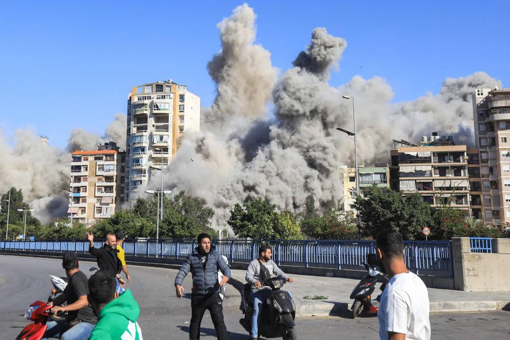 People watch as a smoke cloud erupts after a rocket fired by an Israeli war plane hit a building in Beirut's southern suburb of Shayah on October 22, 2024, amid the ongoing war between Israel and Hezbollah. (Photo by AFP)