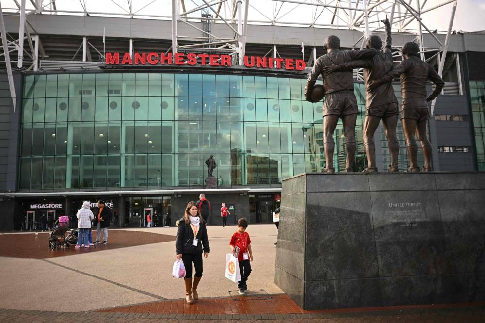 Visitors walk past Old Trafford, in Manchester, north west England, on October 28, 2024. Manchester United sacked manager Erik ten Hag on October 28, 2024 after a disastrous start to the season with former Red Devils striker Ruud van Nistelrooy named interim boss. (Photo by Paul ELLIS / AFP)
