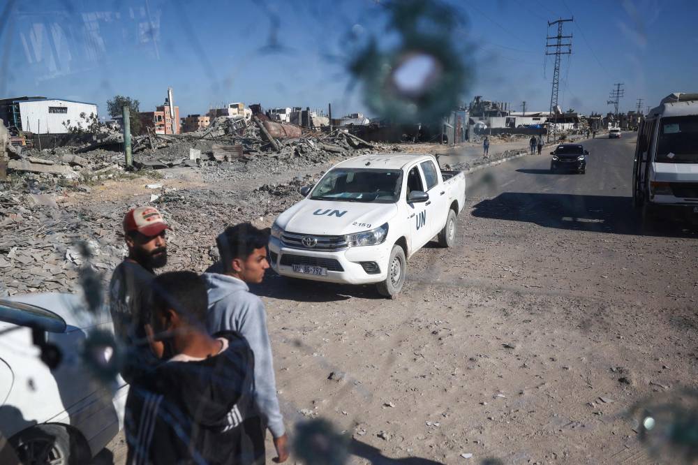 People and a UN Relief and Works Agency for Palestine Refugees (UNRWA) vehicle are seen through the shrapnel-riddled windscreen of a bus that was damaged when an Israeli artillery shell reportedly landed near it on Gaza's main Salah al-Din road, outside Deir el-Balah in the central Gaza Strip, on October 24, 2024, amid the ongoing war between Israel and Hamas. (Photo by Eyad BABA / AFP)