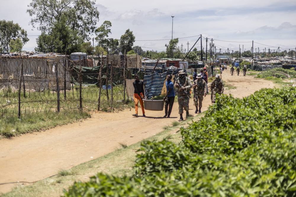 FILE PIX FROM 2023 - Suspected informal miners, commonly known as “zama zamas” (“those who try” in the Zulu language) carry confiscated items while being escorted by South African National Defence Force (SANDF) soldiers during operation Shanela in the Soul City informal settlement near Kagiso on December 14, 2023. (Photo by Roberta Ciuccio / AFP)