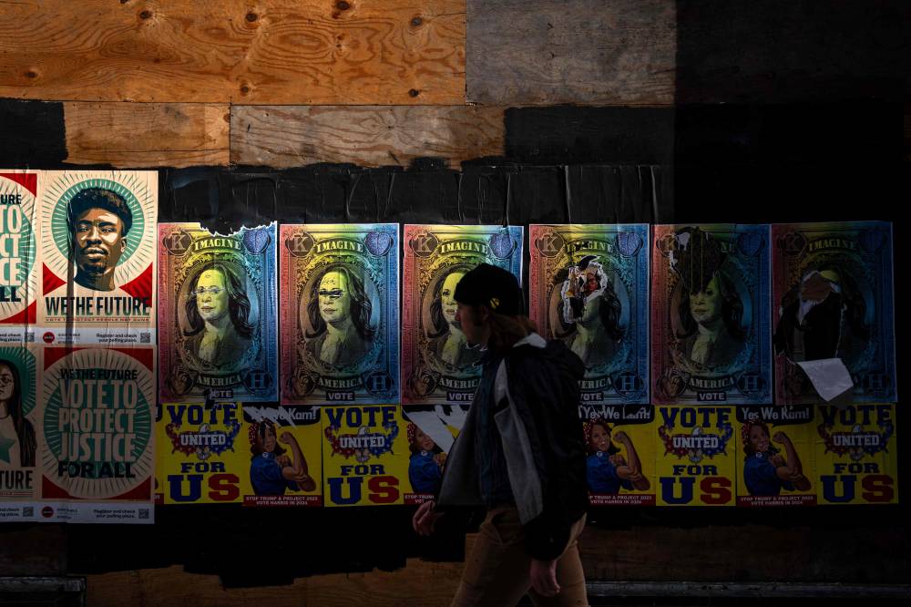 People walk past posters campaigning for Democratic presidential nominee, US Vice President Kamala Harris are seen on a wall along twelfth street on November 04, 2024 in Philadelphia, Pennsylvania. - Photo by AFP
