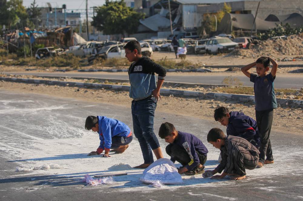 Palestinian boys scrape flour off the ground after a bag fell from an aid truck driving down the Salaheddin road in Deir el-Balah in the central Gaza Strip on Nov 5, 2024 amid ongoing Israeli attacks. - (Photo by EYAD BABA / AFP)