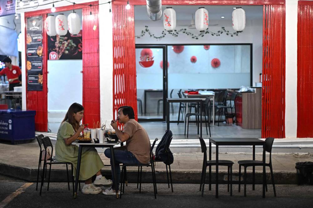 A couple eat at an eatery along a street in Bangkok on November 3, 2024. (Photo by MANAN VATSYAYANA / AFP)