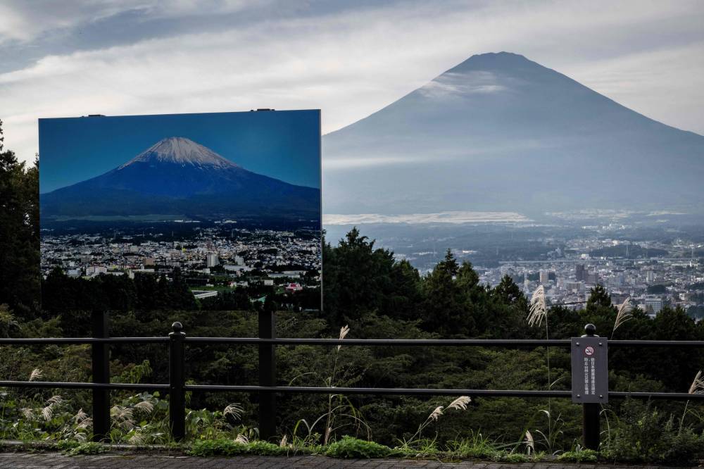 A sign with a photo of Mount Fuji covered in snow is seen at a view point as Mount Fuji, the highest mountain in Japan at 3,776 metres, looms in the background in Gotemba, Shizuoka prefecture on October 31, 2024. - Photo by AFP