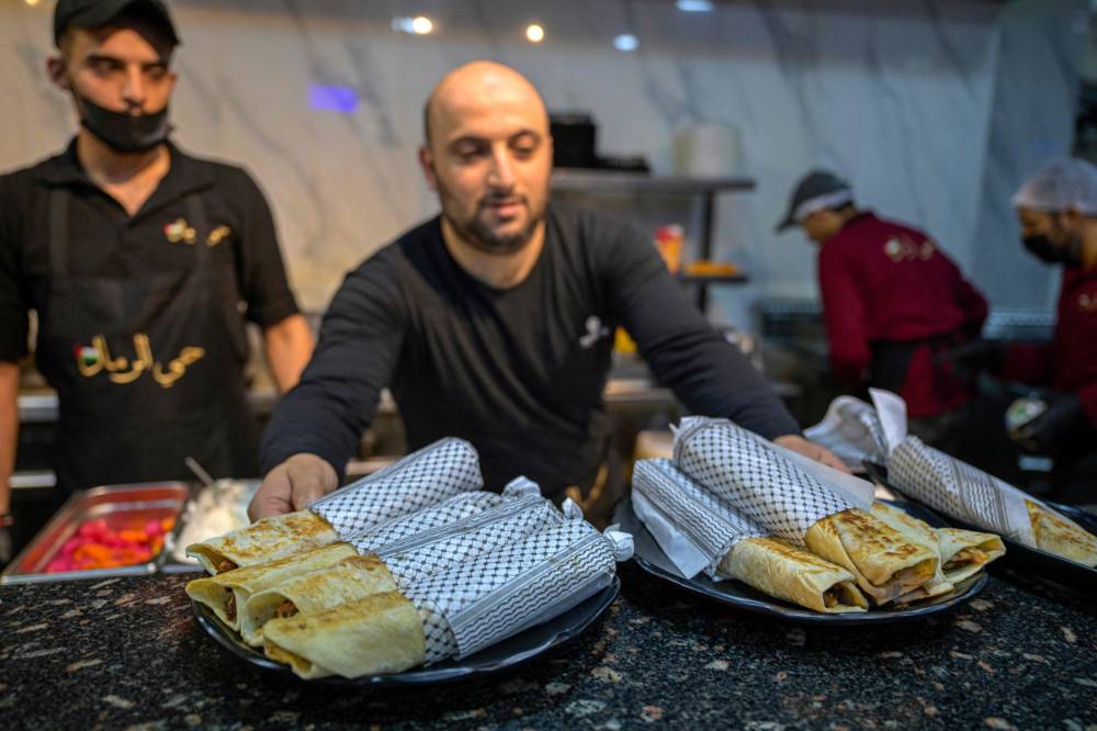 A waiter serves Gaza-style turkey shawarma sandwiches, wrapped in paper with the Kefiyeh pattern, at the 'Hay Al-Rimal' Palestinian-owned restaurant in Cairo. Photo by Khaled Desouki/AFP