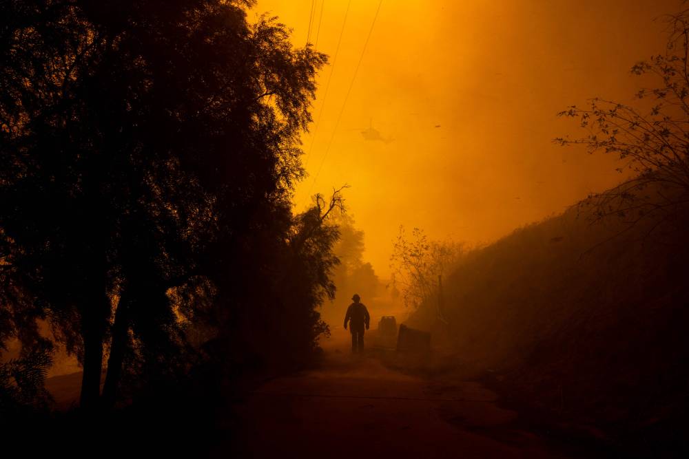 A firefighter walks on a path engulfed in smoke and embers as high winds push the Mountain Fire in Camarillo Heights, Camarillo, California, on November 6, 2024. (Photo by ETIENNE LAURENT / AFP)