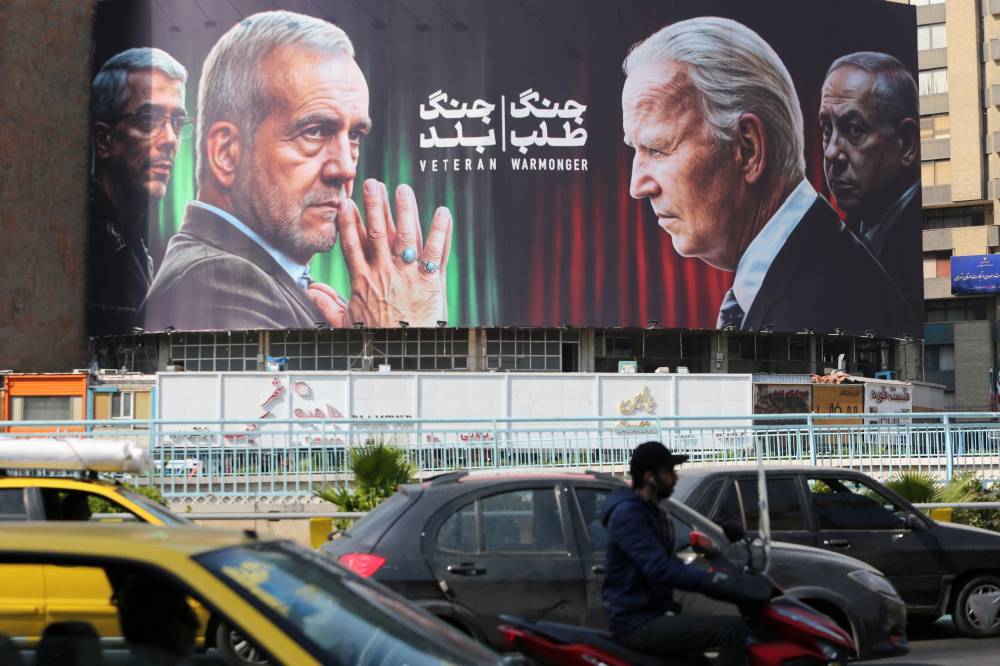 Commuters drive past a billboard bearing pictures of Iran's President Masoud Pezeshkian (second, left), armed forces chief of staff Major General Mohammad Bagheri (left) US President Joe Biden (second, right) and Israeli Prime Minister Benjamin Netanyahu (R) in Vali-Asr square. Photo by Atta Kenare/AFP
