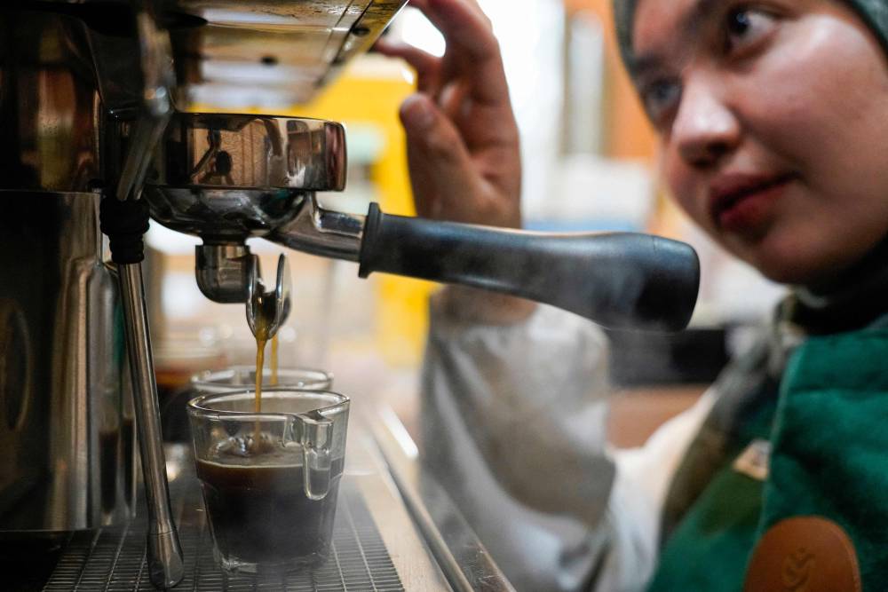 In this picture taken on November 11, 2024, Morning Mama owner Qurrata Ayuni, who lost her parents in the 2004 tsunami, makes a coffee at her cafe in Banda Aceh. - Photo by AFP
