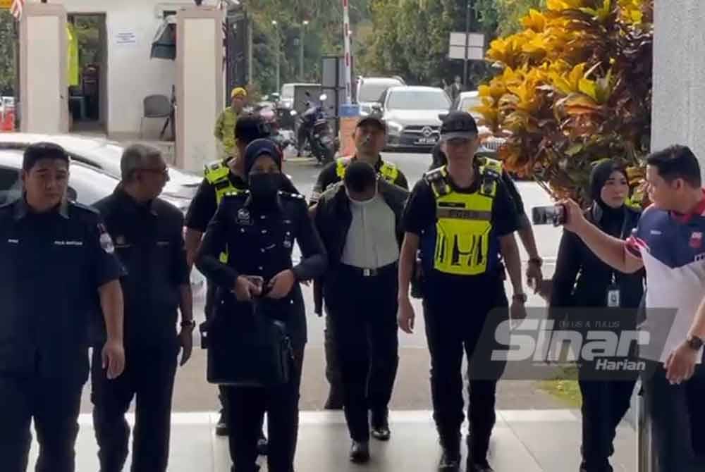 The suspect wearing a white shirt was brought to court accompanied by several police officers to face charges of injuring a first-year UPNM student recently. 