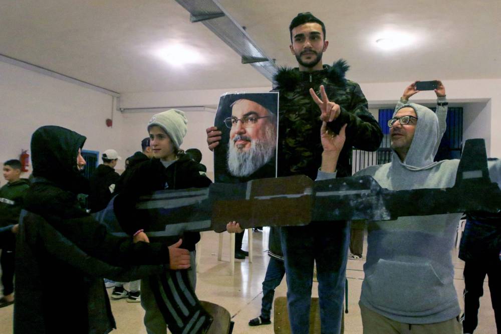 Internally displaced Lebanese hold a portrait of late Hezbollah leader Hassan Nasrallah as they celebrate the announcement of a ceasefire, at a school where they are taking shelter in the southern Lebanese city of Sidon on November 26, 2024. - Photo by AFP